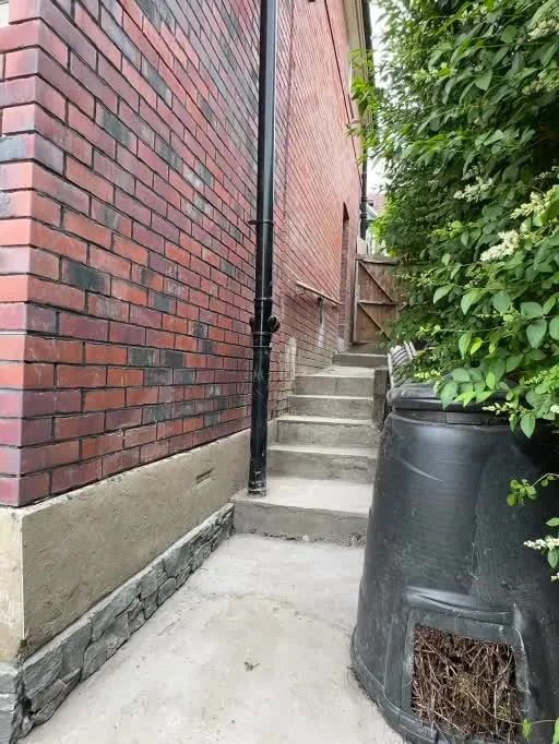 Completed side access beside the red-brick exterior, with concrete steps and a rainwater butt.