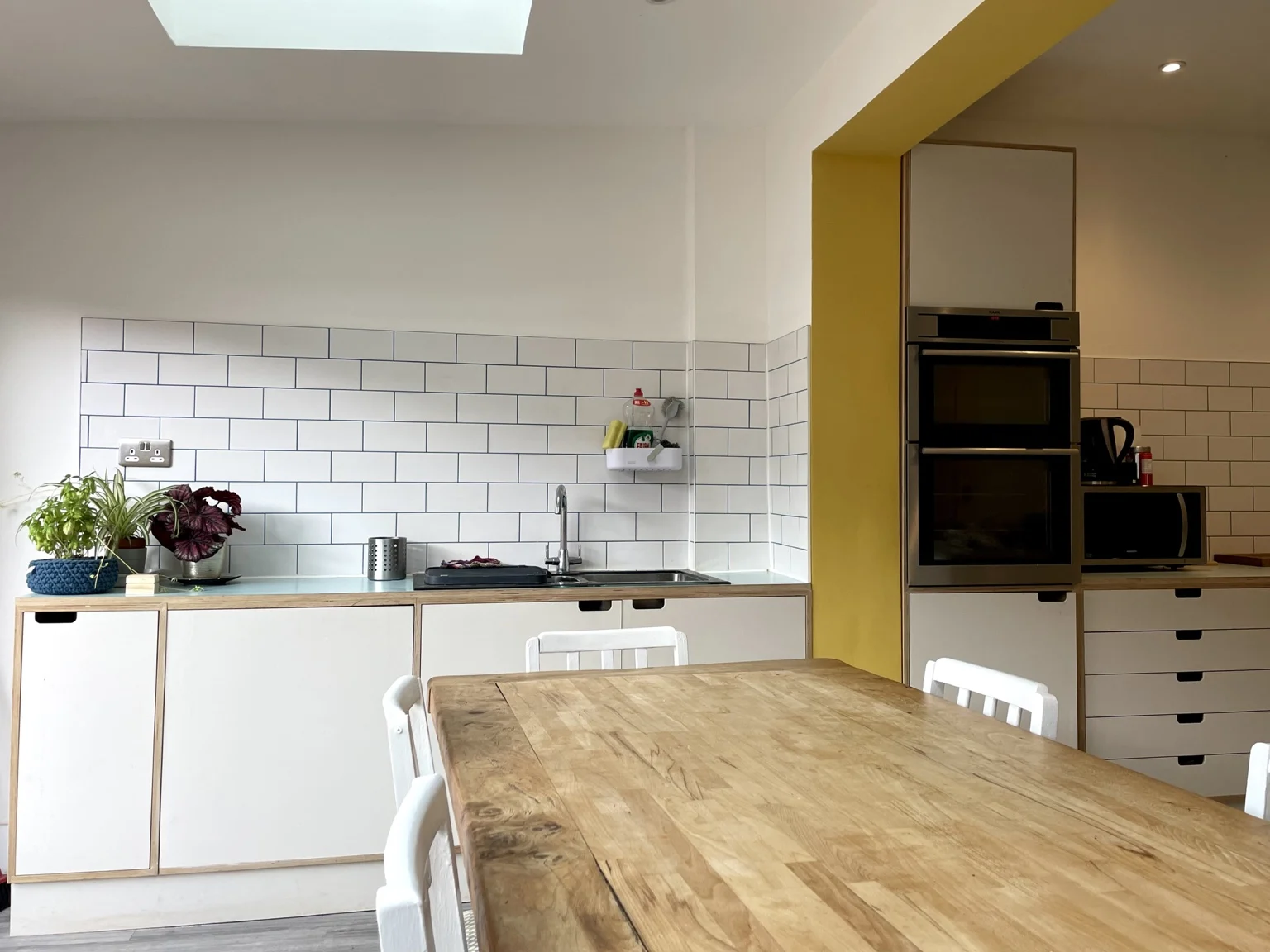Light kitchen cabinetry, timber worktop and dining table beneath a rooflight.