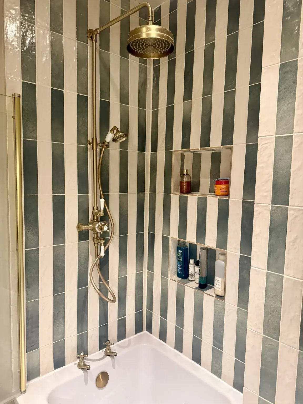 Green-and-cream shower wall tiles with recessed shelving and brass-coloured fittings.